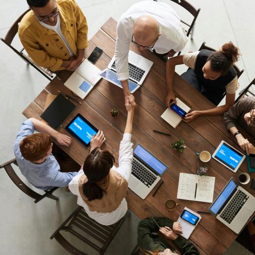 Aerial shot of six people working together at a large table, with note pads and electronic devices.